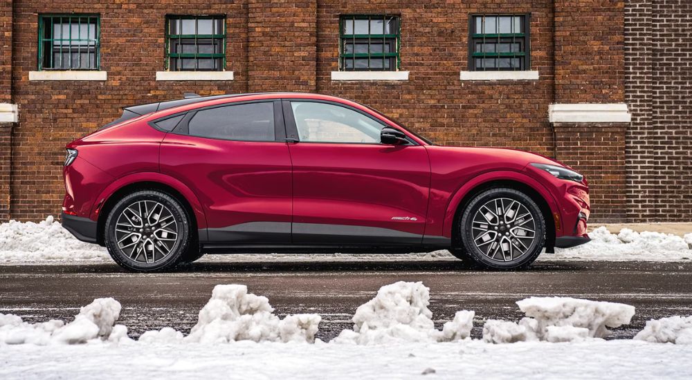 A red 2025 Ford Mustang Mach-E parked on a city street near snow piles.