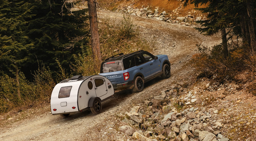 Blue 2026 Ford Bronco Sport towing a small camper on a dirt road