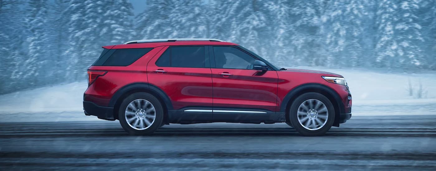 Side angle view of a red 2023 Ford Explorer Limited driving on a snowy road.