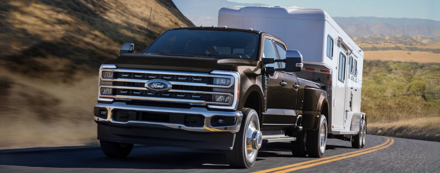 Black 2026 Ford F-350 Lariat towing a trailer down a road.