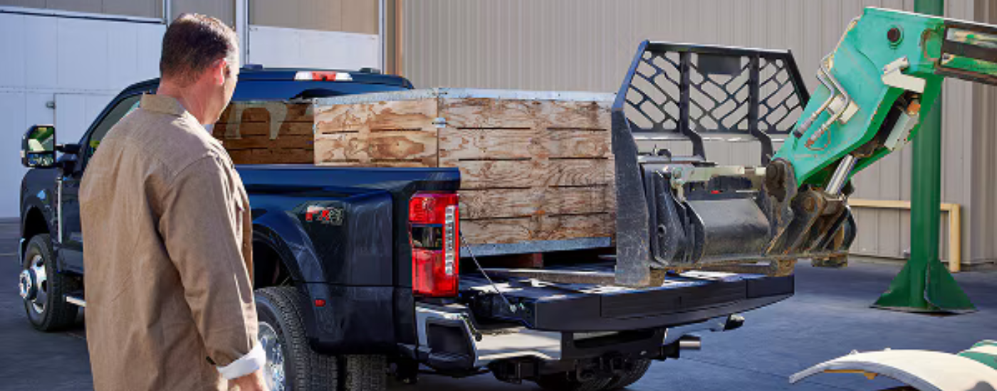 Blue 2026 Ford F-350 with the bed being loaded with a crate