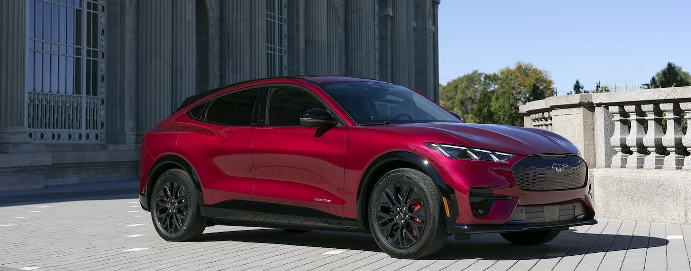Side of a red 2026 Ford Mustang Mach-E parked in front a building.