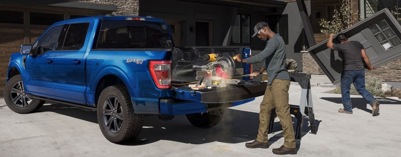 A man operating a saw out of the bed of a blue 2024 Ford F-150 Sport.