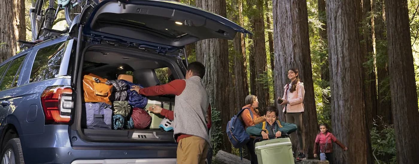 A family is getting camping gear out of the back of a blue 2022 Ford Expedition.